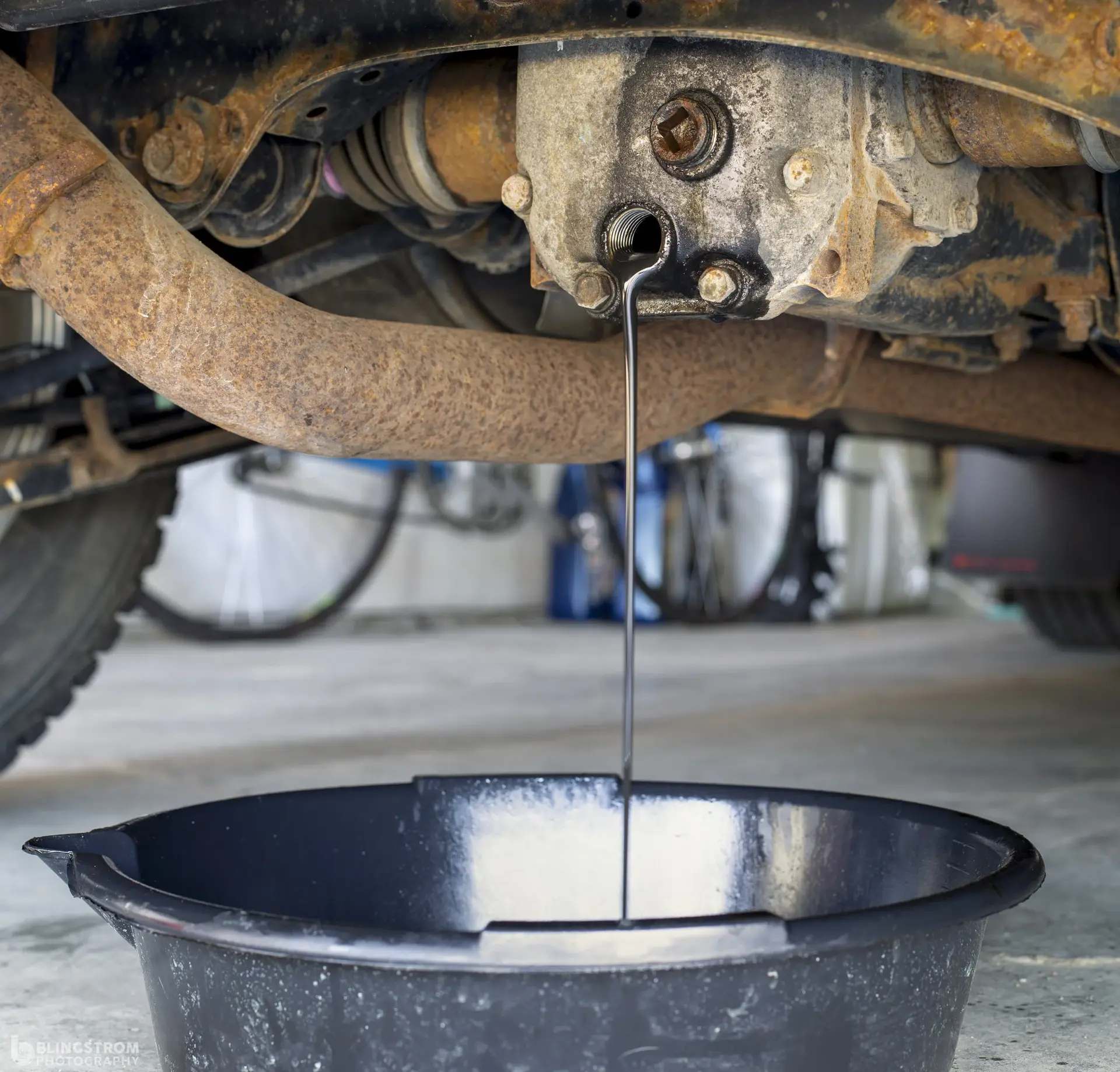 Old dark differential fluid draining into a pan during an Acura SH-AWD rear differential service