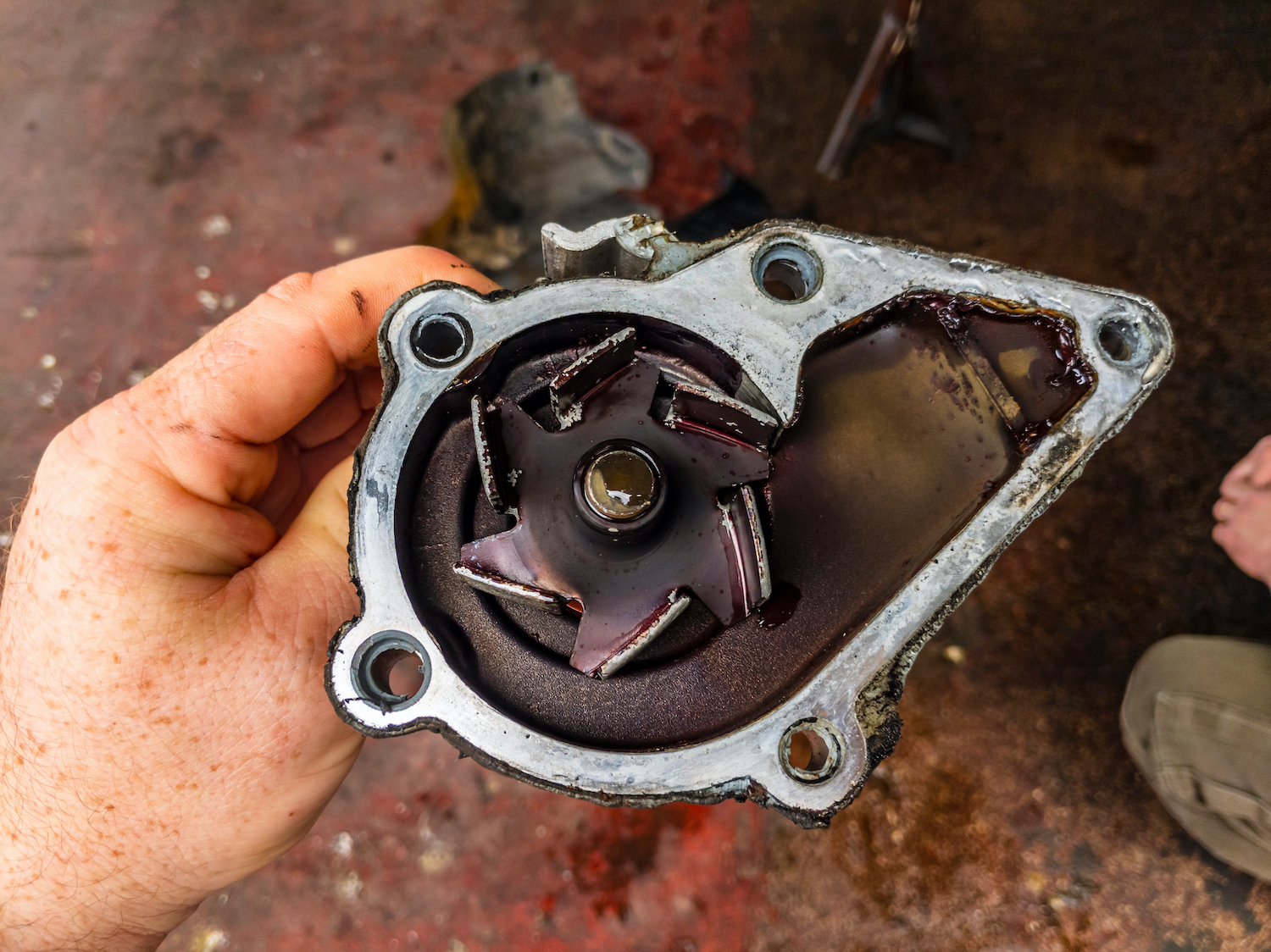 An automotive technician holding a corroded and dirty water pump